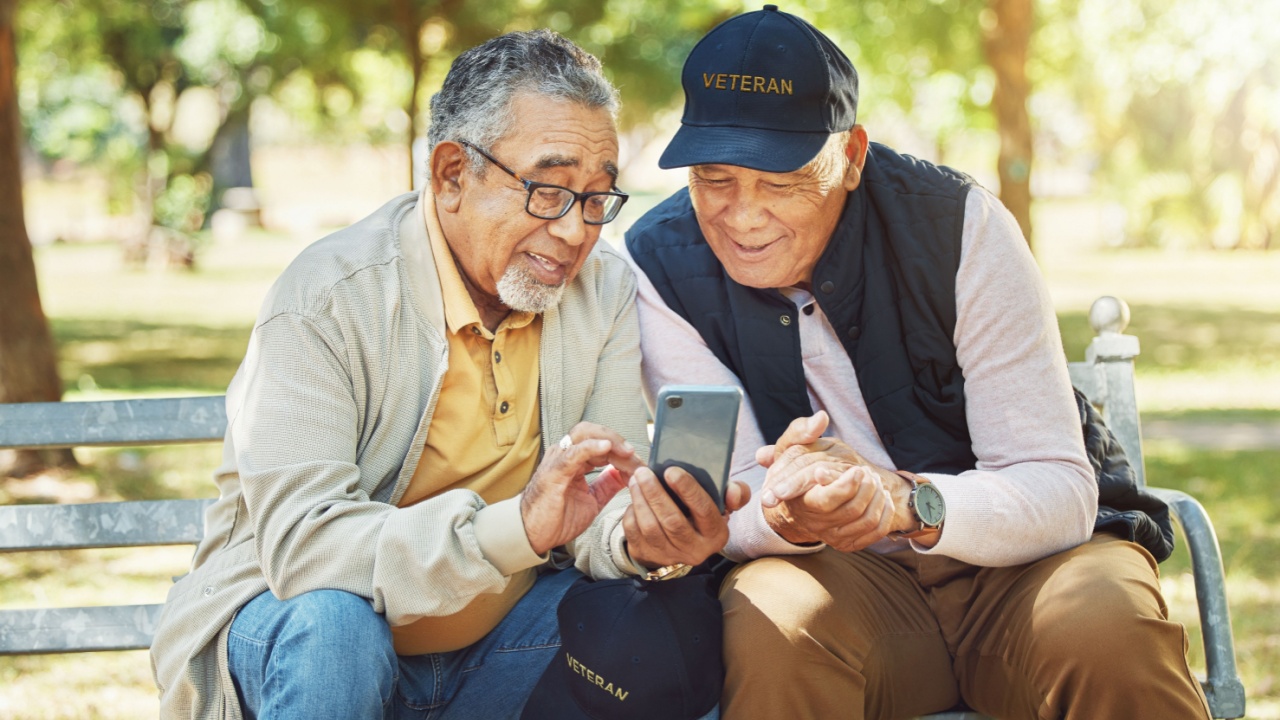 Elderly men, friends and phone in park, reading and army memory with thinking, relax and sunshine. Senior military veteran, smartphone social media and talk on bench, nostalgia and remember service