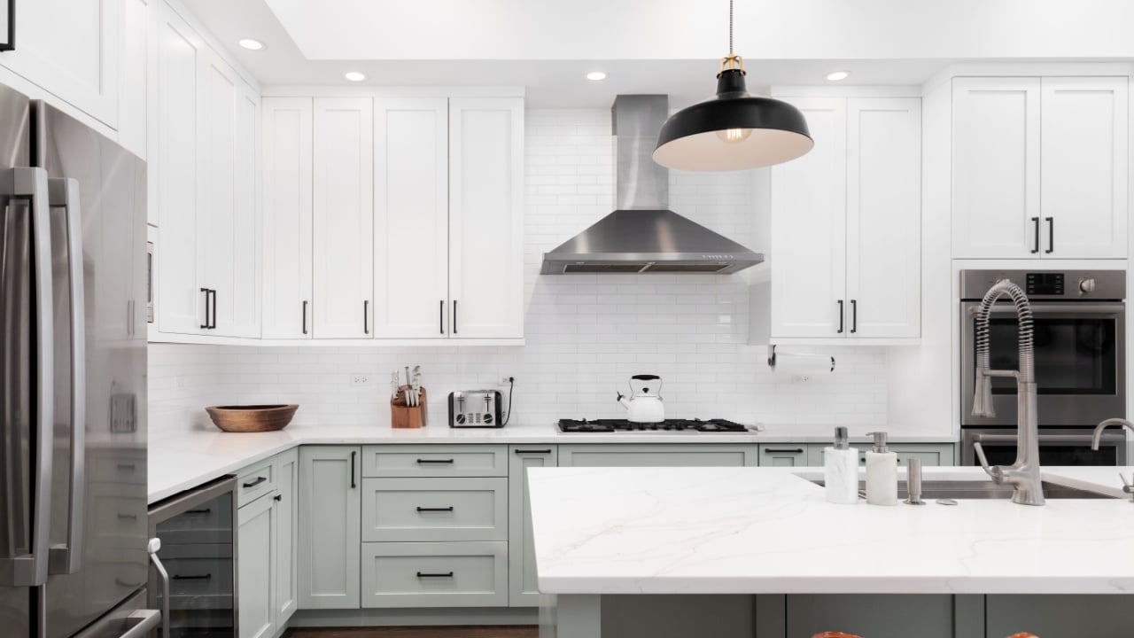 A kitchen detail with white and sage green cabinets, a large island, subway tile backsplash, and stainless steel appliances.