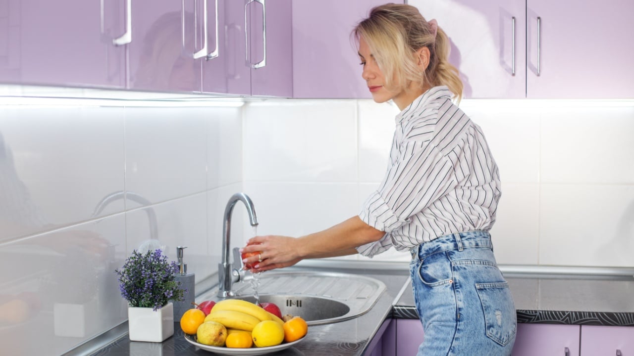Woman washing fresh fruits in kitchen sink. Housework, cooking concept. Organic food.