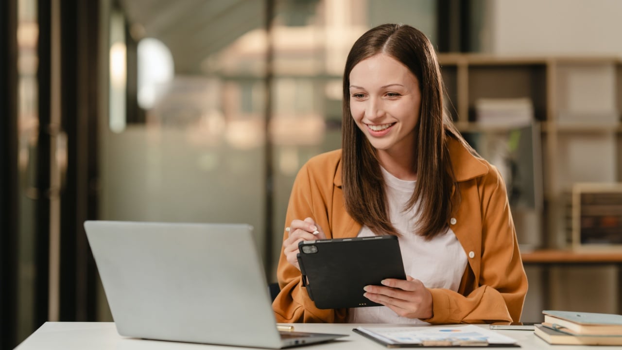 smiling Caucasian university student with a tablet, engaging in online learning, possibly studying liberal arts.