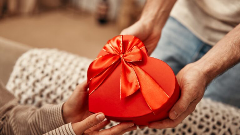 Happy Valentine's Day. A man gives a heart-shaped gift box to his beloved woman in the living room at home. Romantic evening together.