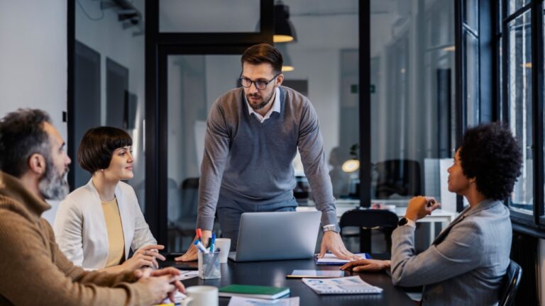 A boss is standing at meeting room with his multicultural colleagues and having important meeting.