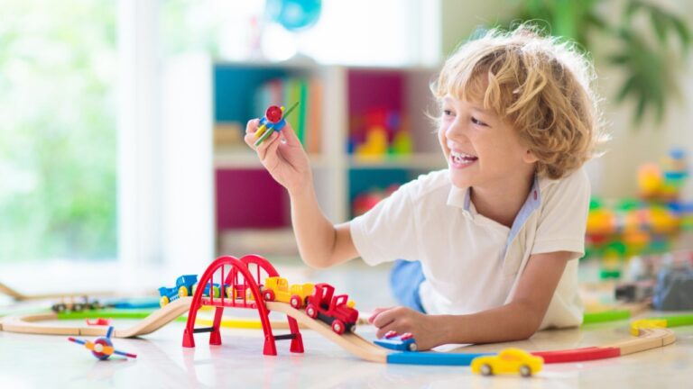 Kids play with toy train railway. Child playing with colorful rainbow wooden trains. Toys for little boy. Preschooler building rail road at home or daycare, preschool. Kindergarten educational games.