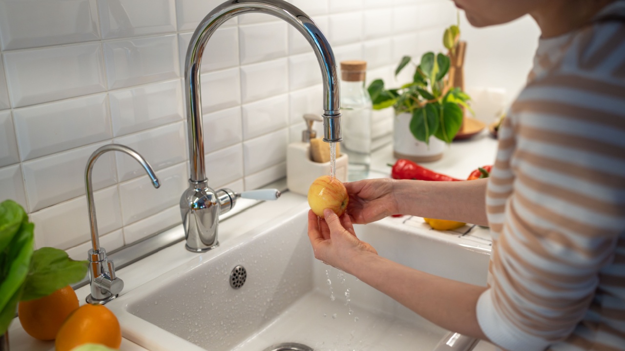 Female thoroughly washing fresh yellow apple in tap water to clean from food wax covering. Nutritional supplements prolonging fruit storage life. Oranges, banana lying on table. Healthy useful food