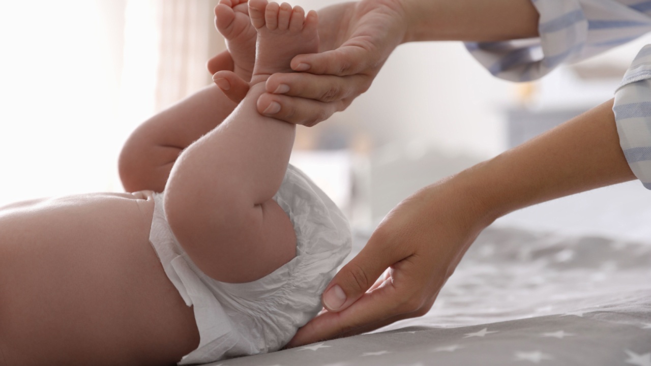 Mother changing her baby's diaper on bed, closeup