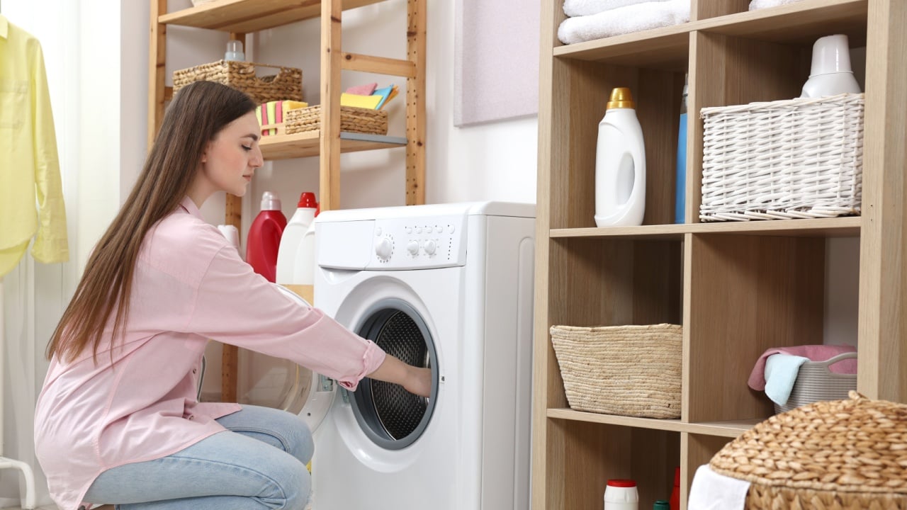 Beautiful young woman near washing machine in laundry room