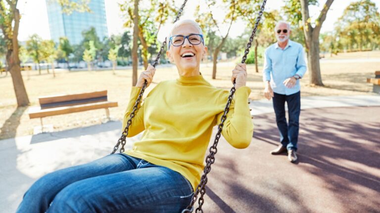 Happy active senior couple having fun on a swing in park outdoors