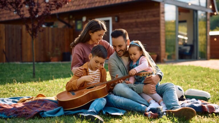 Little boy playing acoustic guitar while enjoying with his family in the backyard. Copy space.