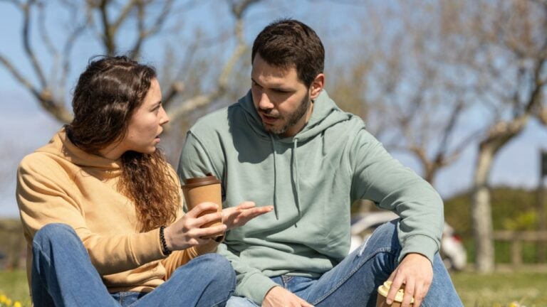 couple in park arguing because they disagree. Young couple on a sunny day arguing about housework or work. Couple talking seriously outdoors in a park.