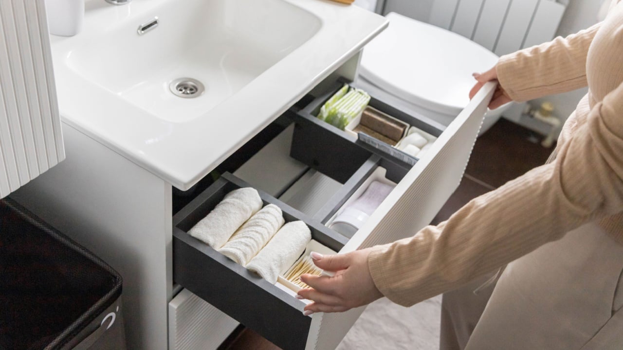 Top view of woman hands neatly organizing bathroom amenities and toiletries in drawer or cupboard in bathroom. Concept of tidying up a bathroom storage by using Japanese method.