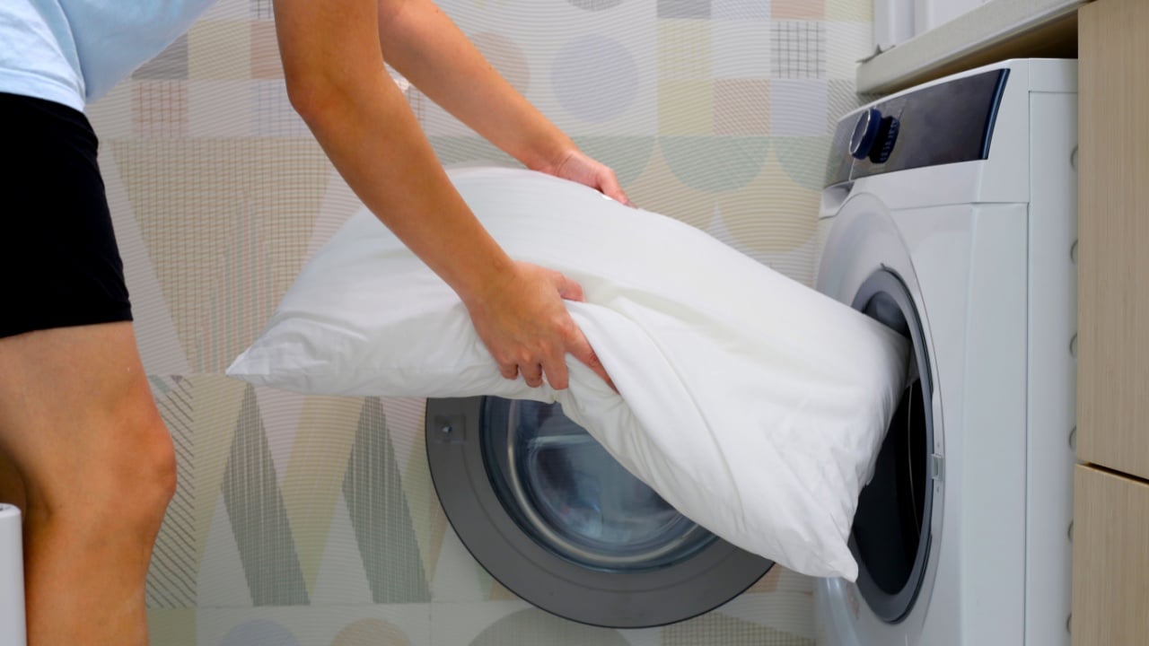 Man's hand holds a pillow and puts it in the washing machine.