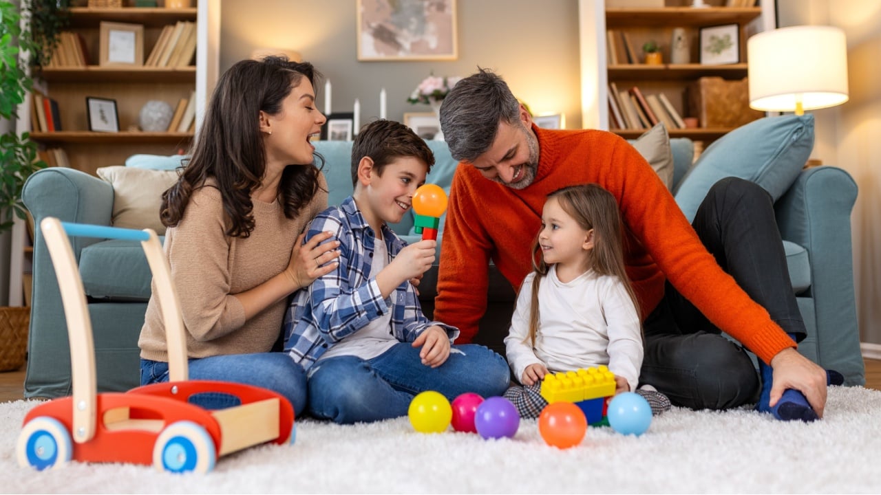 Happy family having fun with toys, parents and little children sit on sofa together, Happy family sitting on sofa playing together. Cheerful parents playing with their kids at home.
