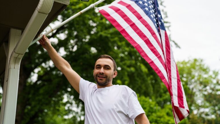Adult man fixing the flag on his house wall.