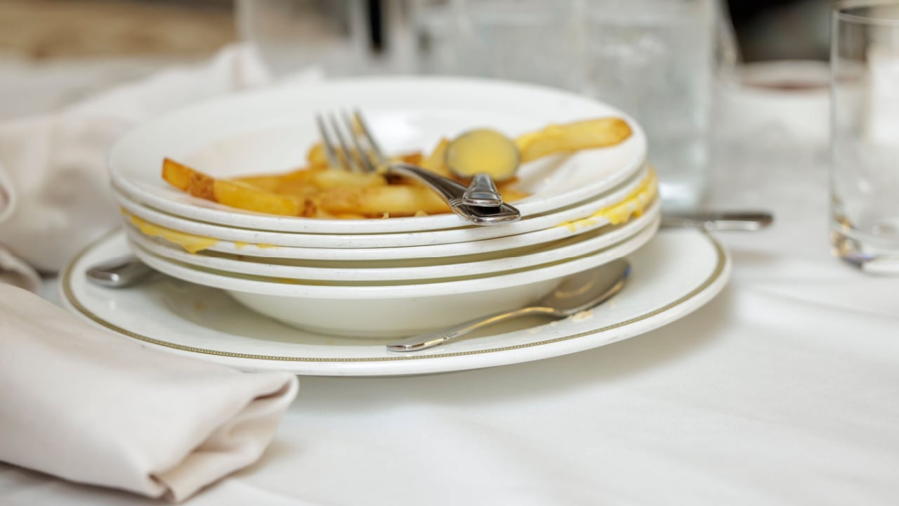 Stacked dirty plates with cutlery after a meal on a white tablecloth at a restaurant table.
