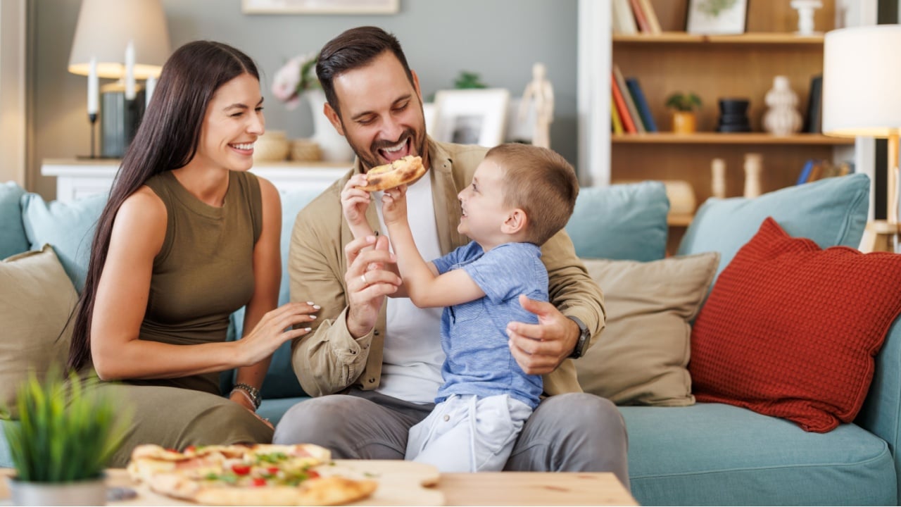Mom, dad and son are eating together at home. Happy family eating pizza at home.