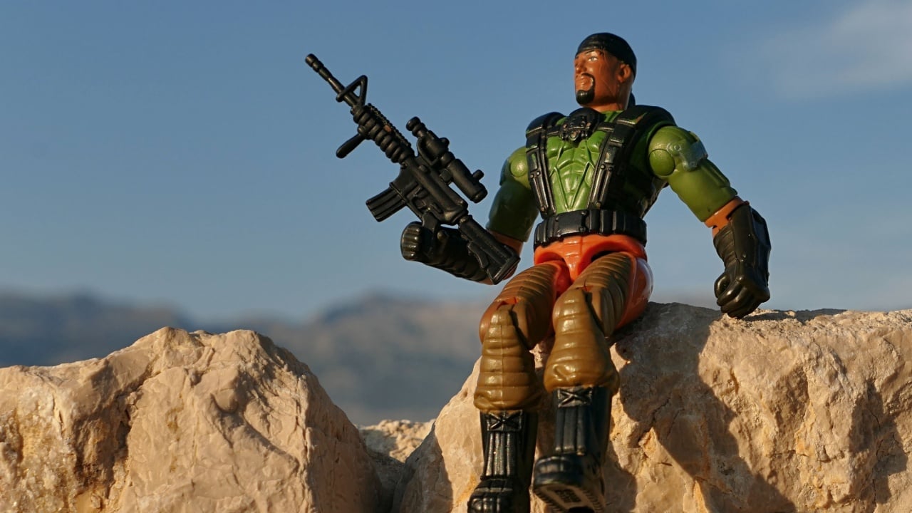 RAZANAC, CROATIA - AUGUST 25, 2024: GI JOE action figure of ordnance trooper Heavy Duty, version 2004 by Hasbro, sitting on coastal rocks with M4 assault rifle with front handle and scope