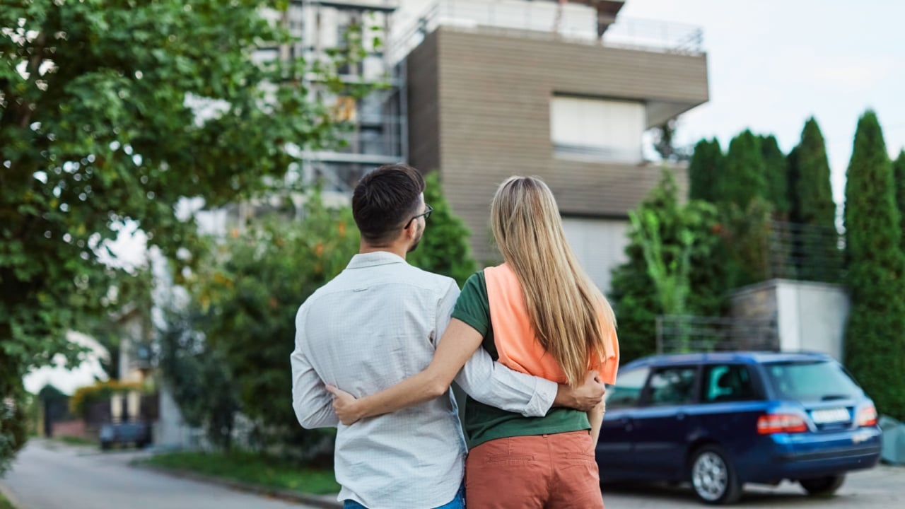 Portrait of a happy young couple standing in front of their new house, with keys in hands, smiling man and woman posing near modern home, making selfie, real estate agency, house owners, young family
