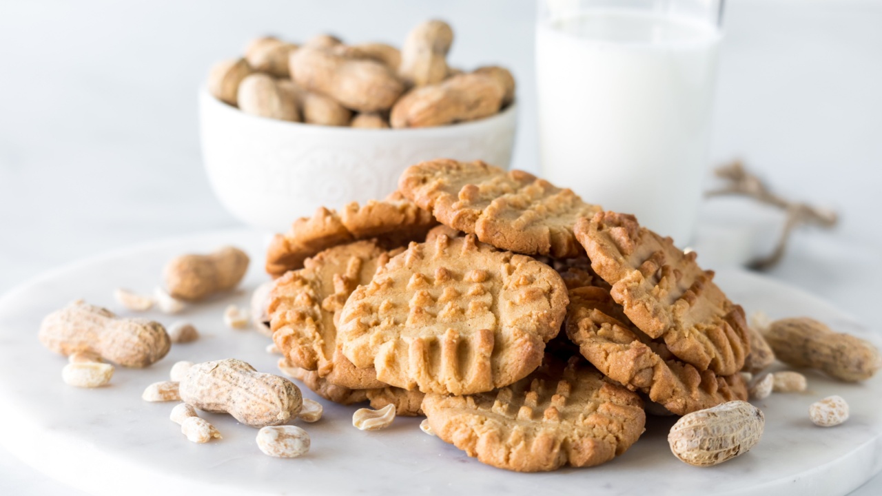 A pile of fresh homemade peanut butter cookies surrounded by peanuts.