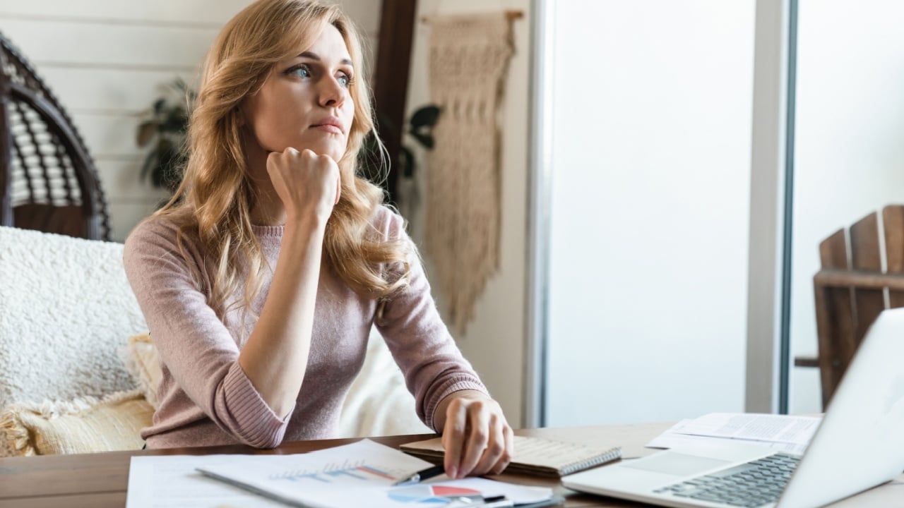 Tired overworked smart Caucasian business woman female manager freelancer sitting at desk working remotely on laptop computer while spending time at home thinking about vacation holidays