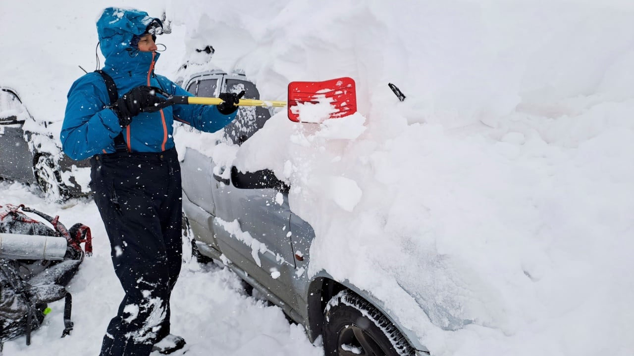 Traveling to the mountains in winter: woman uses a shovel to remove the snow that completely covers her vehicle, in Mendoza, Argentina.