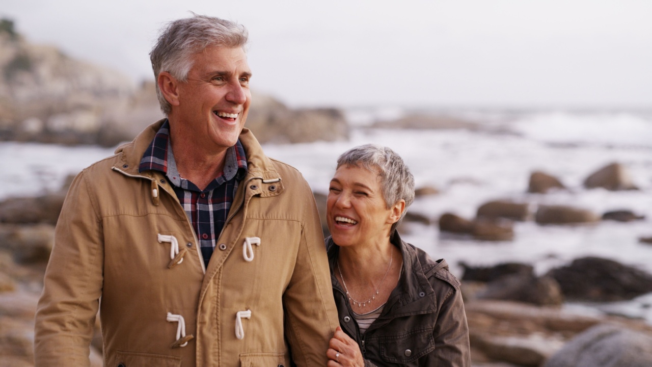 Happy, laughing and senior couple by ocean for bonding, relationship and love in nature. Walking, marriage and man and woman by sea for romance, commitment and relax together on weekend in winter
