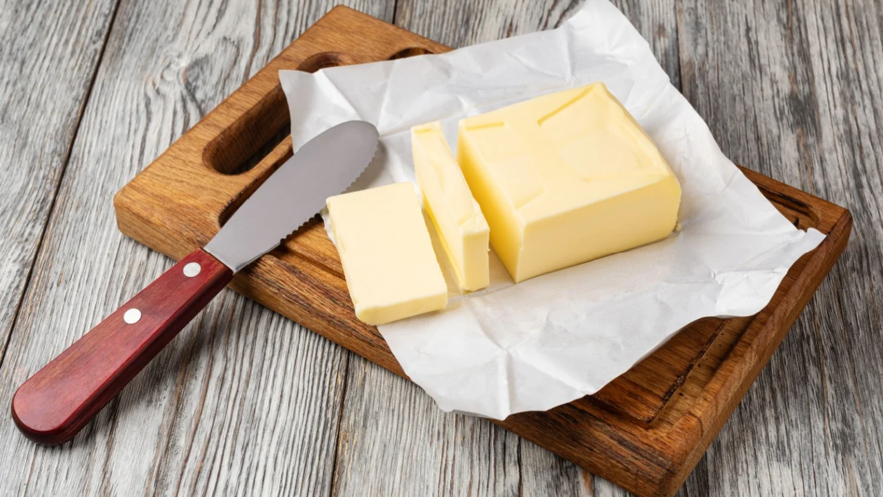 Fresh butter slices on a wooden cutting board with a butter knife, ready for spreading