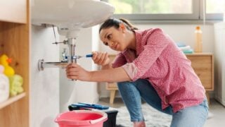 Skilled young woman fixing the bathroom sink by herself using water pump pliers, DIY concept