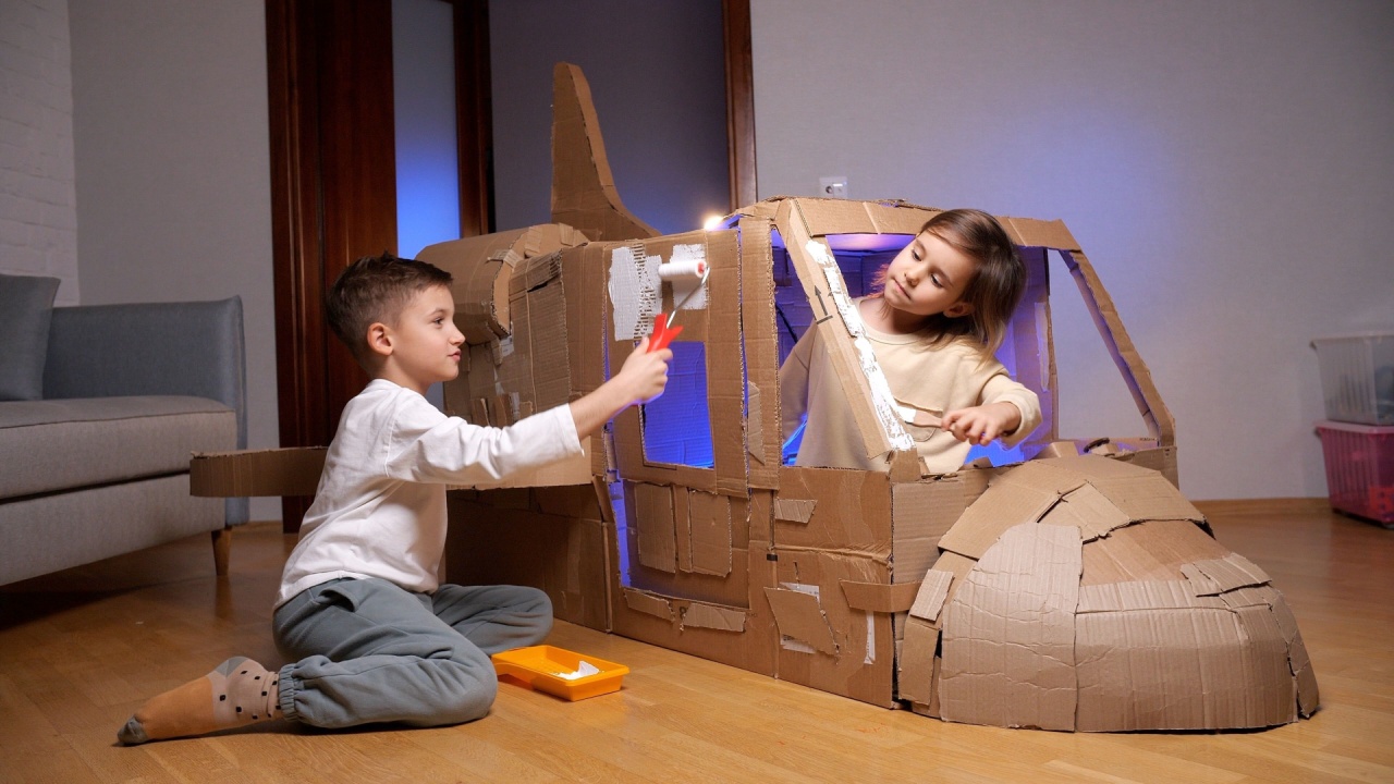 Two young children painting a cardboard spaceship they built together. They are adding a fresh coat of white paint to their cardboard creation