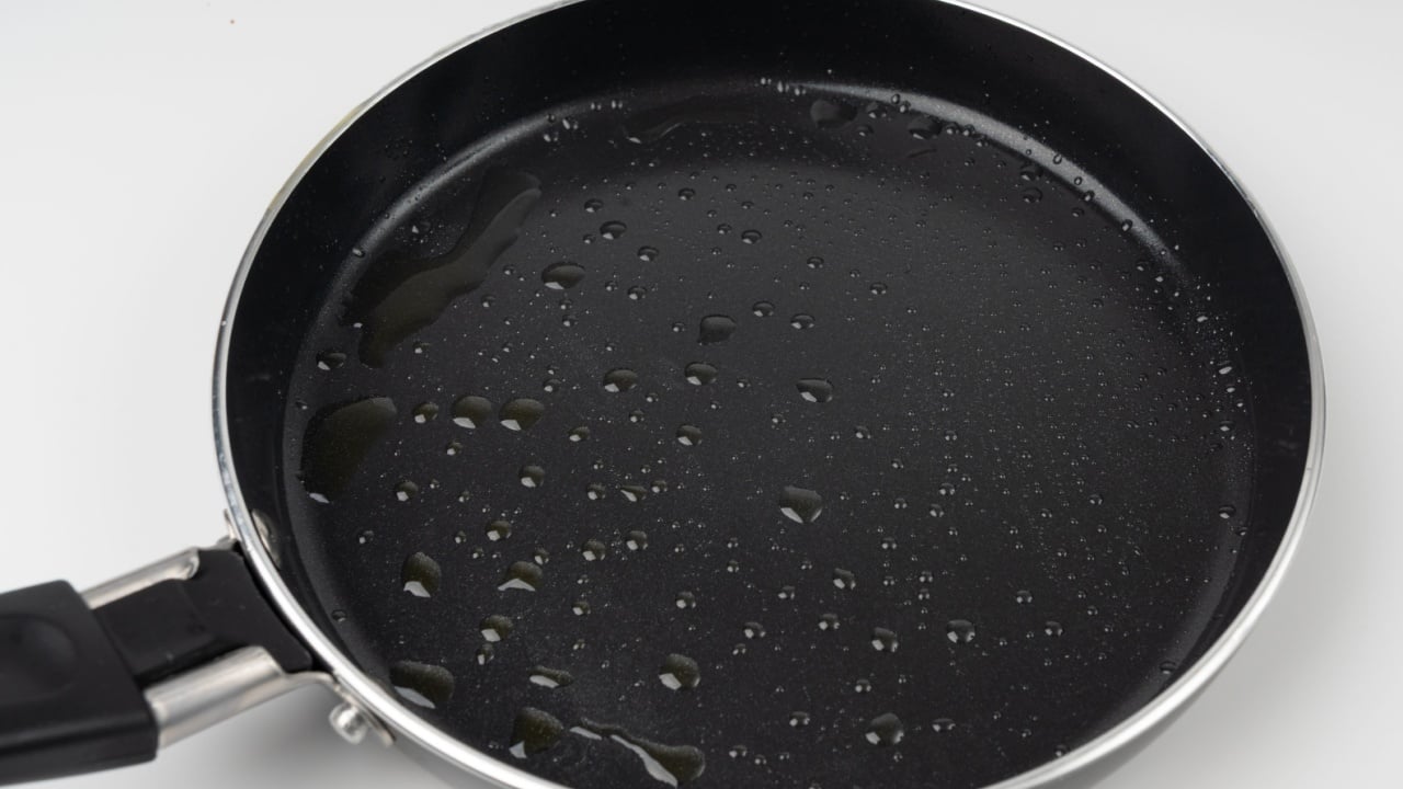 Oil drops on frying pan texture, water splash on black non-stick coating, drop on non stick mini griddle, oily nonstick surface fryingpan on white background