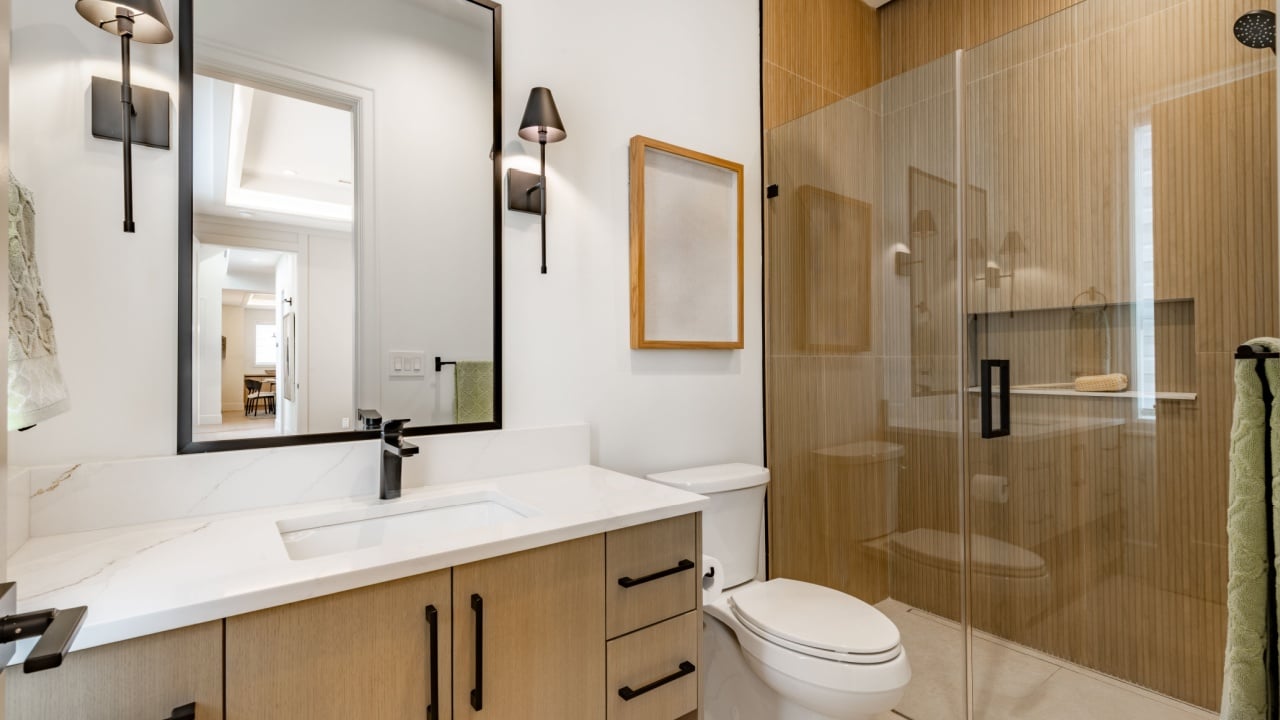 Large elegant bathroom interior with wooden cabinets white granite marble countertops bathtub mirror wall sconce lighting floor lighting glass wall shower black fixtures window with blinds covering