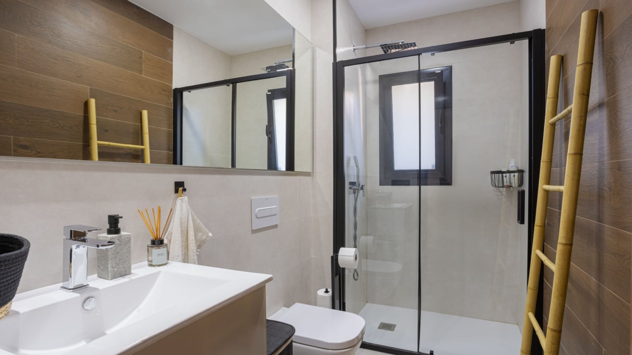 Stylish bathroom featuring a large walk-in shower with glass doors, dual ladders for towels, and warm wooden accents on the walls.