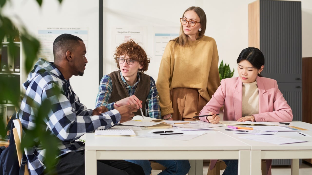 Group of diverse students actively studying foreign languages in a classroom, collaborating and sharing insights at a white table with materials spread out