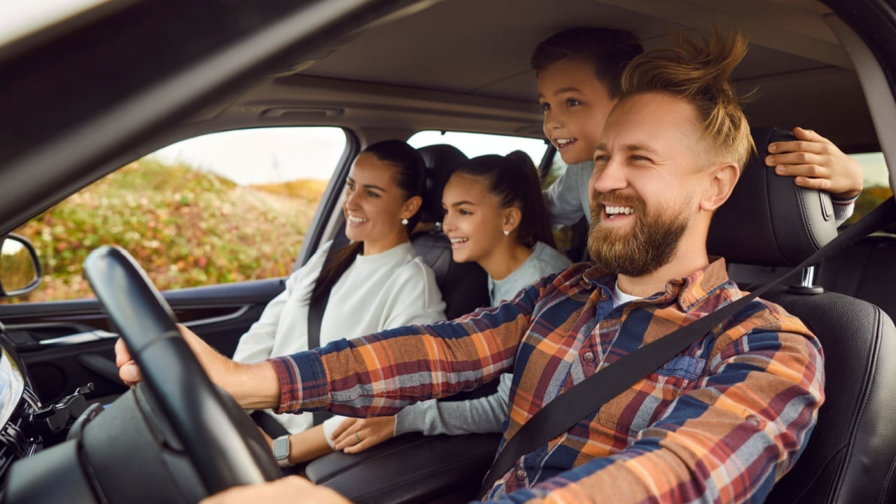 Portrait of happy laughing smiling family of four with children riding in modern car traveling by automobile together enjoying vacation or road trip on weekend. Family travel concept.