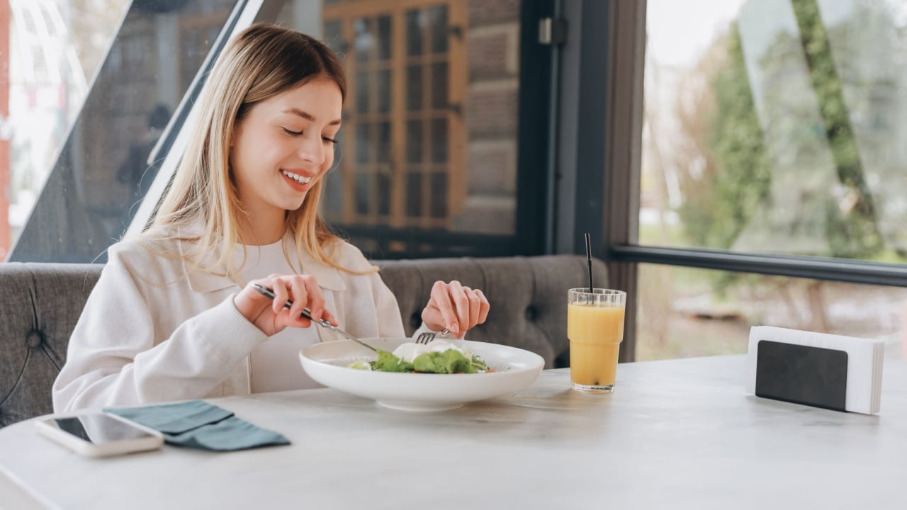 Happy businesswoman eating fresh salad with mozzarella cheese and drinking orange juice, enjoying healthy lunch break in modern cafe