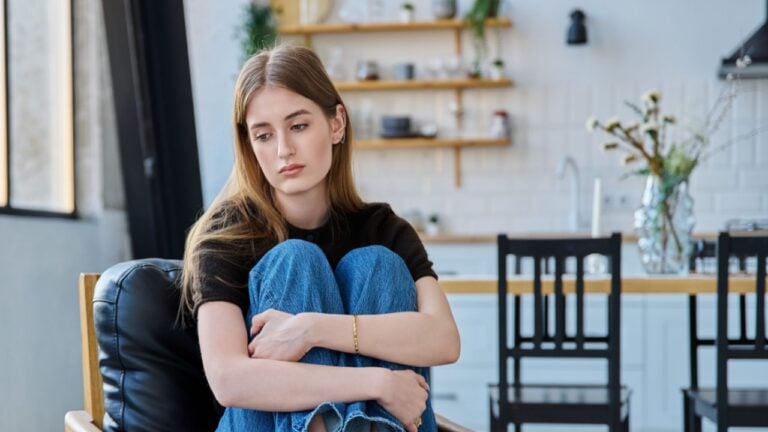 Sad stressed young woman sitting at home on armchair