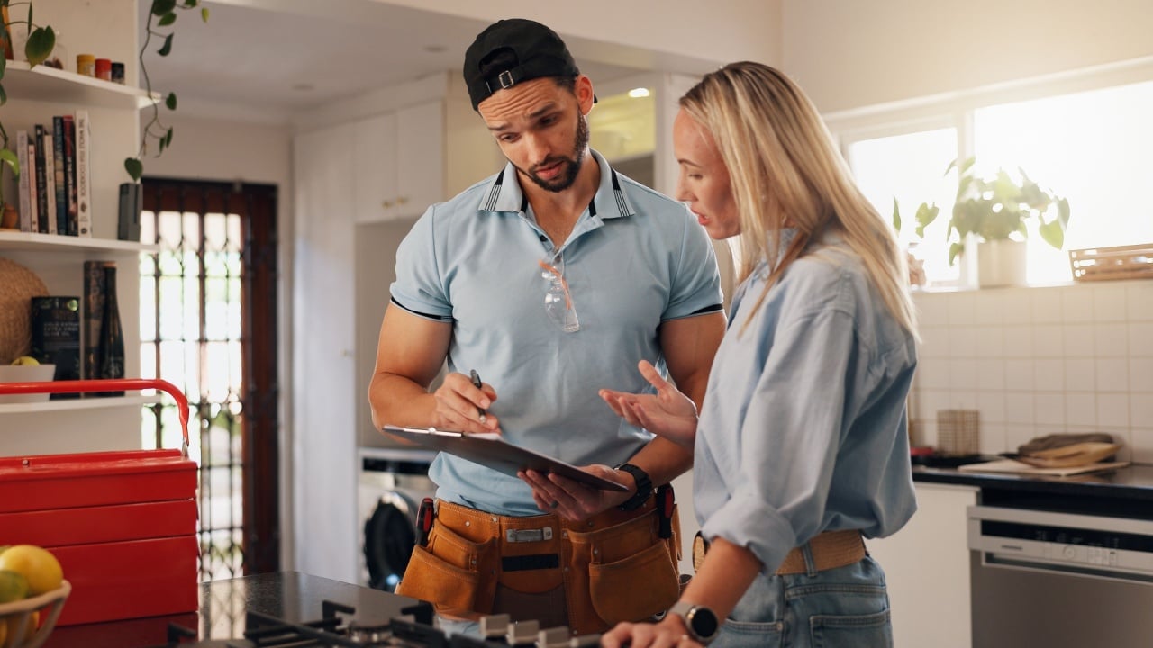 Woman, man and plumber with clipboard in kitchen for invoice, report and talk for repair at house. People, handyman and client with checklist for drainage system, inspection and leak at apartment
