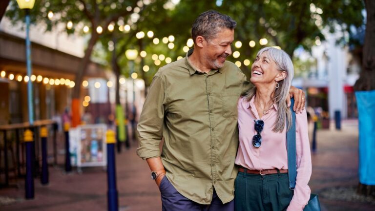 Happy multiethnic man and smiling woman enjoy a romantic evening outdoors. Mature couple shares a loving moment while walking in a european city.