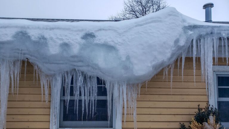 large pile mound of snow hanging off over the side, corner of a roof following a winter snowstorm, icicles, building, window, cold, frozen, white