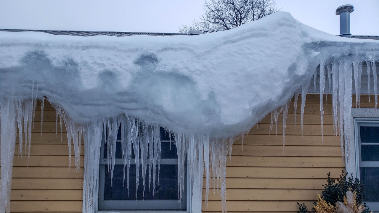 large pile mound of snow hanging off over the side, corner of a roof following a winter snowstorm, icicles, building, window, cold, frozen, white
