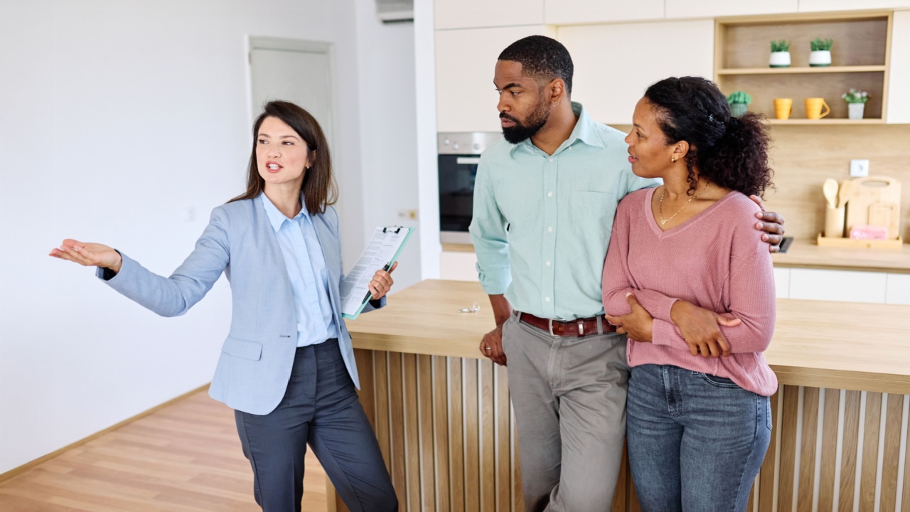 Female Real Estate Agent Selling And Showing The Modern Apartment kitchen To His Young Clients, young couple That Are Standing Next To her In The Fancy Apartment