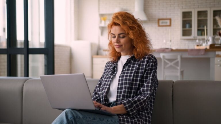 Smiling Caucasian woman female lady freelancer girl student e-learning working business online internet computer typing laptop internet shopping buying purchase at home couch web chatting technology