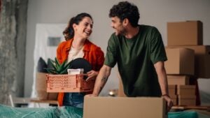 Young couple moving into their new apartment, joyfully carrying boxes and plants, sharing smiles and excitement for their fresh start
