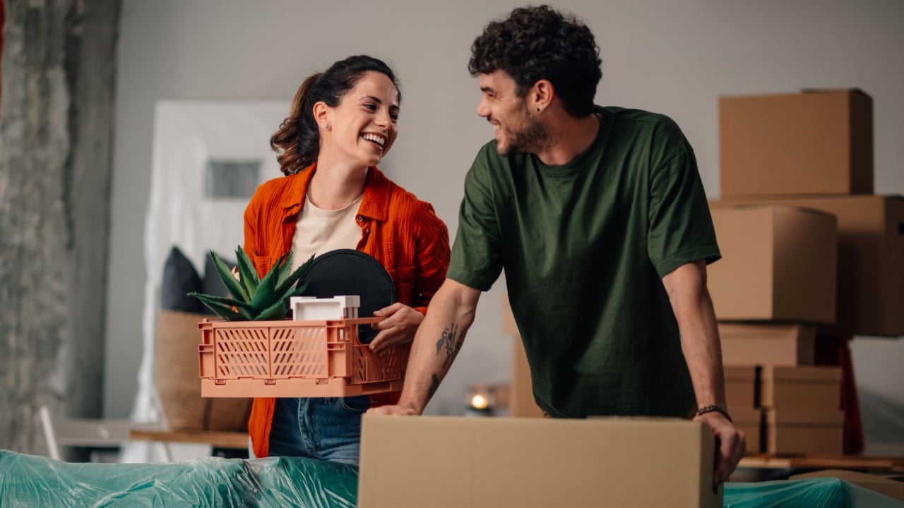 Young couple moving into their new apartment, joyfully carrying boxes and plants, sharing smiles and excitement for their fresh start