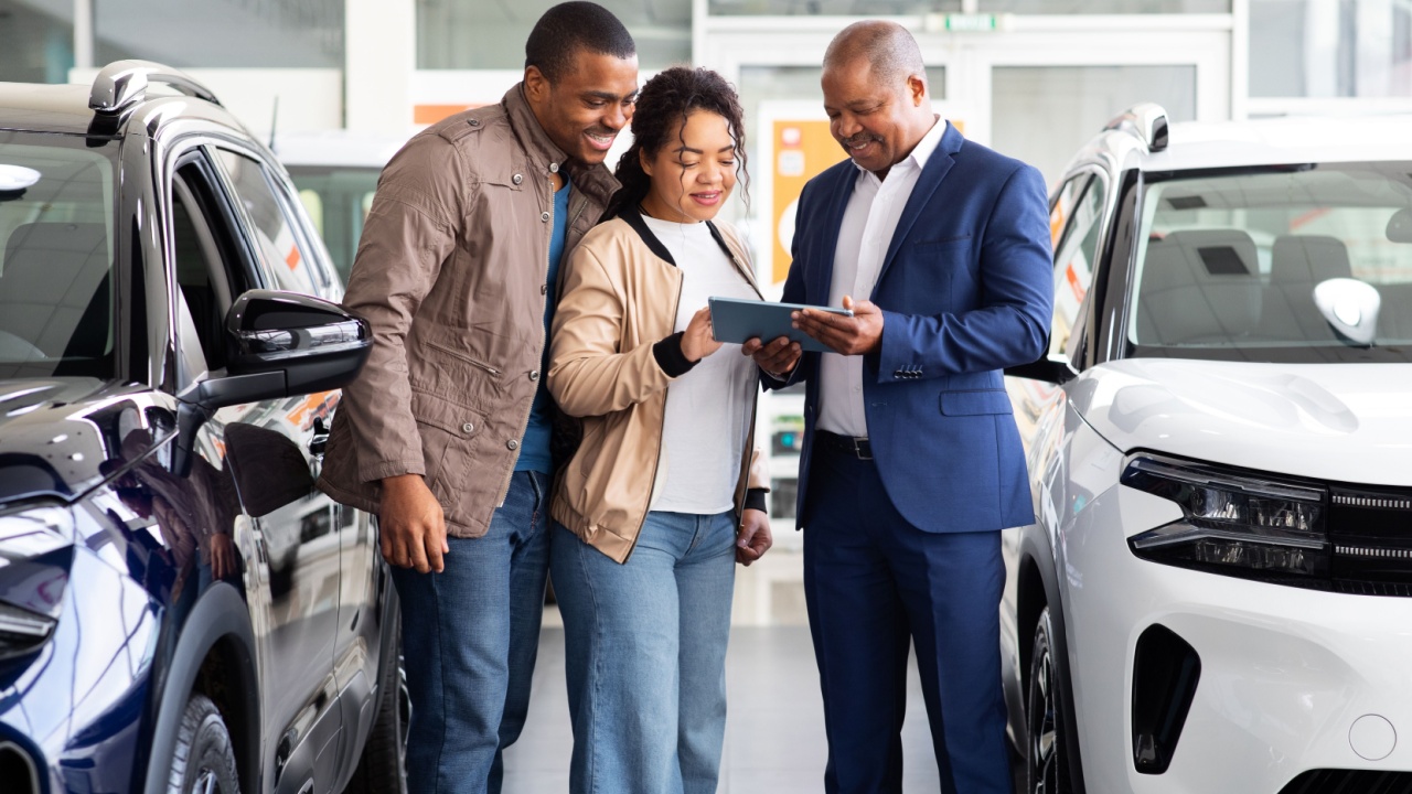 Car dealer showing digital tablet to smiling African American couple in showroom