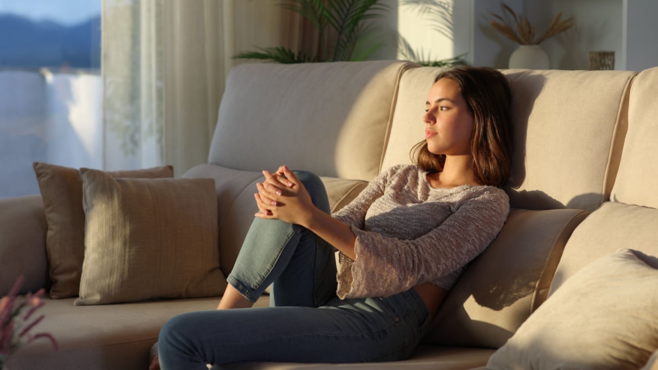 Woman thinking sitting on a couch at home looking away through a window