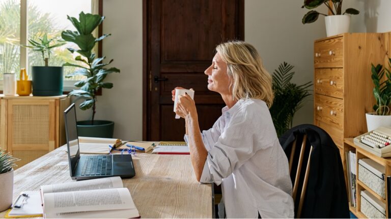 Thoughtful blond haired business woman relaxing drinking hot drink tea a desk of her workplace in office