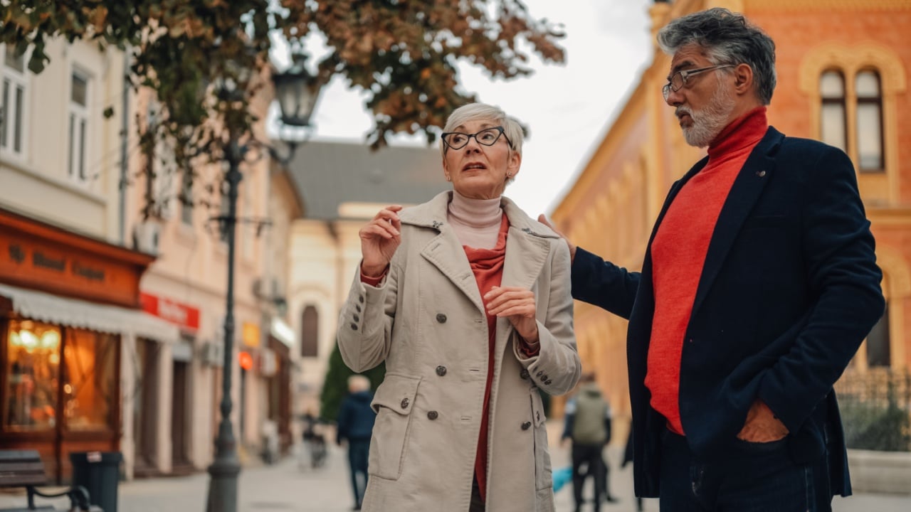 Elegant senior couple visiting a new city, getting lost and asking for directions, during a beautiful autumn day