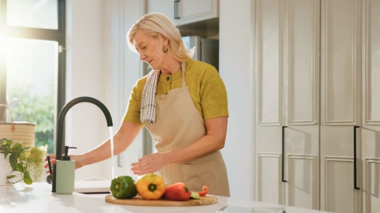 Senior woman, rinse vegetables and kitchen with cleaning, dirt removal and faucet for dinner at house. Person, wash pepper and ingredients with cooking, diet or hygiene for nutrition in retirement