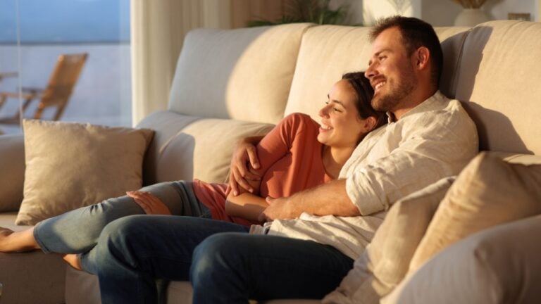 Happy couple enjoying sunset together sitting on a sofa at home