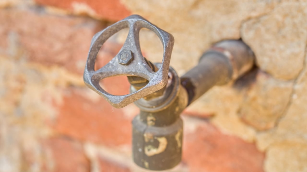 Close-up of a rusty outdoor water faucet against a brick wall.